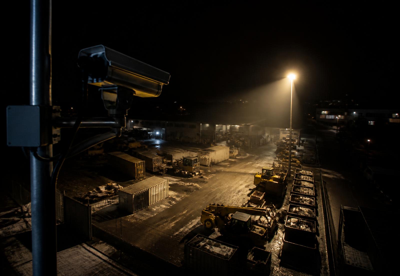 Security camera monitoring a commercial equipment yard at night under floodlights
